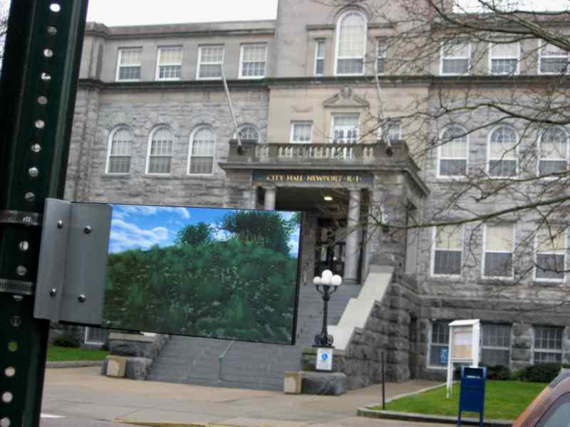 A photo of a building with a sign in front of it. The sign has a photo of "Renew Field", which is a 3D rendering by Rupert Nesbitt.